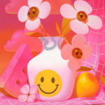 Painting of a pink tablescape containing a watermelon slice, a peach, pink flower, and a white vase with a yellow smiley face containing three flowers whose centers are skulls by Megan Ellen MacDonald