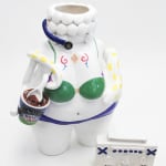 Ceramic body wearing a green bikini top and blue bikini bottoms. They are holding an open tub of Ben and Jerry's ice cream with a spoon in it. There is a snake wrapped around their shoulders and a black head piece microphone on their head. There is a small boombox next to them on the floor.