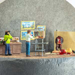 Miniature diorama by Abigail Goldman of a man painting a portrait of two dead bodies while another man is filming