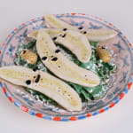 Ceramic sculpture of a bowl of bananas cut in half with faces and two peanuts with faces on a bed of lettuce
