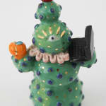 Jen Dwyer sculpture - green cactus figure with one eyeball at center holding a laptop and other accessories