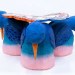 Sculpture of three blue birds holding a plate of food and various things on their backs