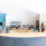 miniature diorama by Abigail Goldman depicting three scenes, two people dead in a bathroom, a laboratory and a family watching tv
