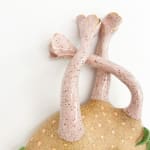 detail shot of sculpture by Jen Dwyer of light pink tentacle like objects emerging from brown mound with green leafs