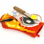 Ceramic sculpture of a lobster claw shaped oven mitten with a lobster shaped plate on top of it. On top of the plate is a knife with butter, an ace of spades playing card and a wet wipe.