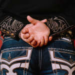 Photo of a persons back with embroidered jeans and black longsleeve shirt with their hands behind their back