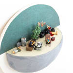 miniature diorama by Abigail Goldman of two people sitting around a table covered in paper and dead bodies in the background