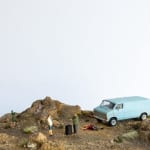 miniature diorama by Abigail Goldman of two man standing next to a burn barrel and a dead body on the dessert