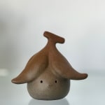 Bronze sculpture of a figure with a peeled banana on its head in brown
