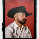 Photo of a man with a beard wearing a black cowboy hat and a white shirt on a red background