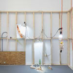 white wall with wooden scaffolding with dog human sculptures displayed in various scenes such as hanging from a chord and eating pizza