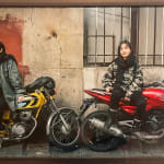 Photo of two women sitting on red and yellow motorcycles in wooden frame
