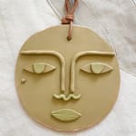 flat ceramic face with a cloth loop for hanging at the top