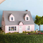miniature diorama by Abigail Goldman of a woman running over a body with a lawnmower in the front yard of a pink house