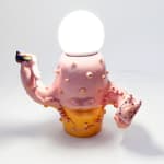 Lamp sculpture of a cactus like object with lips and two arms holding a plate with a sandwich and the other a bag of chips