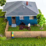 miniature diorama by Abigail Goldman of two boys looking over a fence into the yard burying dead bodies