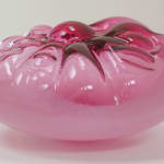 Side view of a dark-pink, cushion-like blown-glass sculpture.
