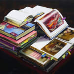 Stacks of books with colorful covers and many Post-it notes sticking out to mark important pages. Books on top are open, revealing blurry colorful images.