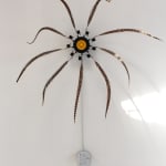 Still image of a moving mechanical wall mounted sculpture made out of a long wires, speakers, multiple long pheasant feathers, and various materials which create a flower like structure