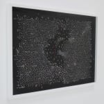 Side view of a framed black, horizontal rectangle with millions of white dots, hanging on a white wall.