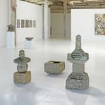 Assortment of Japanese stone sculptures in gallery with colorful paintings on back wall.