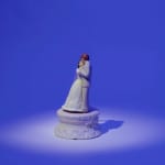 still from video shows bride and groom cake toppers in white dress and suit embracing in spotlight on royal blue background