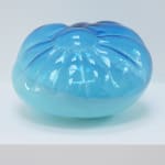 A cushion-like blown-glass sculpture, top two-thirds translucent blue, bottom one-third opaque blue on a white pedestal.
