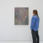 A man stands to the right and faces a multicolored abstract painting hanging on a white wall.