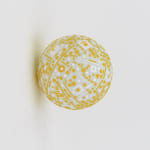 White pingpong ball attached to wall is covered in cut-out geometric shapes of yellow and white paper.
