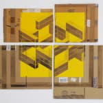 Four pieces of cardboard (all different sizes) are arranged on a wall. The space between them creates a cross. A yellow square is painted on each piece of cardboard with geometric incisions creating an arrangement of stacked shipping containers and revealing the corrugated cardboard.