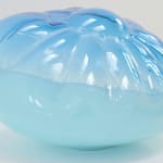 A cushion-like blown-glass sculpture, top two-thirds translucent blue, bottom one-third opaque blue.