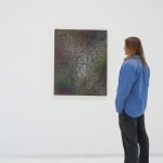 A man stands to the right and faces a multicolored abstract painting on canvas.