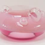 UFO-shaped glass sculpture. Top 2/3 opaque blush-pink, bottom 1/3 pink. Clear top with clear bubbles of varying sizes.