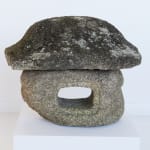 Weathered stone sculpture with open hole in center and sloped edge topper.