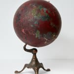 Globe with antique stand. Globe is covered in mostly red with black markings and some spots of greens and yellows, with black markings on top. No recognizable land formations.