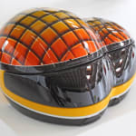 Sculpture of conjoined motorcycle helmet forms that are decorated in red and yellow grid pattern to look like a hornet’s eyes.