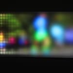 Still image of a rectangular piece with multi-colored LEDs behind angled Plexiglass that display scenes of people running To the right side the scene is burry due to the Plexi being farther away while at the left is it more pixelated due to the Plexiglass being closer