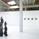 Installation view of Totem with 5 square panel paintings hanging in a horizontal line on the wall behind the sculpture