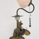 A vintage lamp made of found materials, featuring a canine statuette, pull chain, and flower bud-like bulb