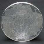 Front view of a clear convex disk with etchings set on a dark grey background.
