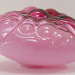 Side view of a dark-pink, cushion-like blown-glass sculpture.