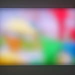 Still image of rectangular piece with multiple multi-colored LEDs behind Plexiglass that displays a blurred and abstract scene of prayer flags flapping in the wind
