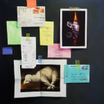 Blurred items taped to dark gray wall, including: pictures of a metal lighter and a sheep and other colorful letters and scraps of paper.
