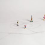 still from video shows winding and circling path drawn on white surface with figurines standing on various point on the path