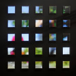 Still image of a spread out grid of twenty five square pieces with multi-colored LEDs behind Plexiglass. The LEDs display pixelated scenes of runners from a marathon