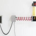 Electronic wall mounted sculpture made out of three different sized LCD screens, red, yellow, and black coiled wires, and custom electronics. On each of the LCD screens an orange, yellow, or pink colored hand holds up a different set of fingers or a fist in order to indicate a number