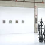 Installation view of Totem with 5 square panel paintings hanging in a horizontal line on the wall behind the sculpture