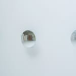 Side angled view of three reflective disks mounted in a row on a white wall.