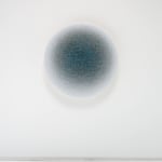 Front view of a blue ombre circle created from overlapping threads hanging on a white wall.