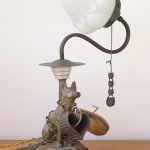 A vintage lamp made of found materials, featuring a canine statuette, pull chain, and flower bud-like bulb